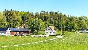 Et landligt landskab med et rødt lade, et hvidt hus og et stort træ i forgrunden.