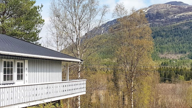 A white wooden house with a balcony, surrounded by trees and a mountain in the background. - 10 Person Holiday Home in Tynset-by Traum (Tynset)