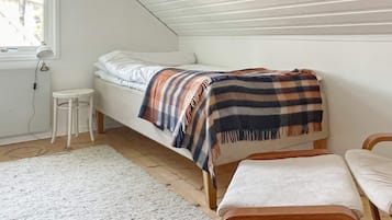 A small, single-bed room with a sloped ceiling, a white wall, a small stool, and a bench.