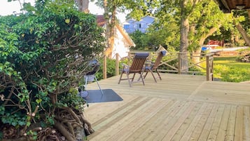 A wooden deck with a grill, two chairs, and a view of houses in the background.