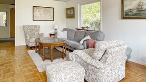 A living room with a sofa, armchair, and ottoman, a glass coffee table, and two framed pictures on the wall. - 4 Star Holiday Home in Branno (Branno)