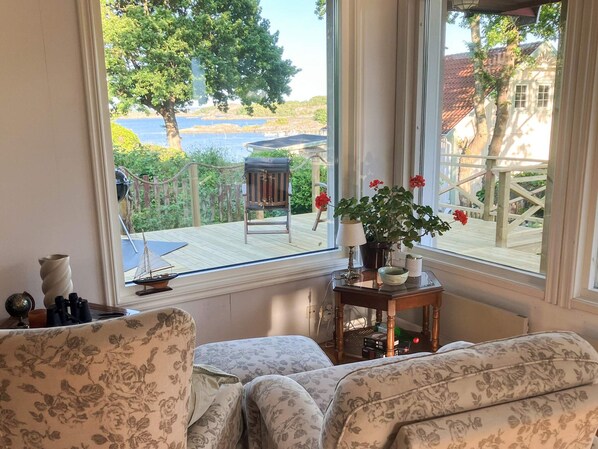 A room with a view of a wooden deck, a chair, a table with a lamp, and a potted plant. - 4 Star Holiday Home in Branno (Branno)
