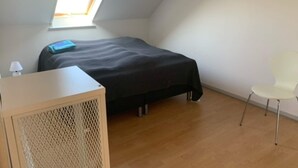 A small, tidy room with a bed, a desk, a chair, and a window.