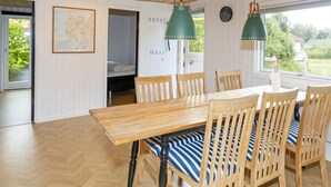 A dining area with a wooden table and chairs, a map on the wall, and a window with a view of greenery. - 6 Person Holiday Home in Farso (Farso)