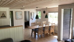 A room with a wooden ceiling, a dining table with chairs, a sofa, and a bed in the background. - 6 Person Holiday Home in Farso (Farso)