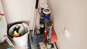 Un angolo di stanza con un secchio, uno straccio e prodotti per la pulizia.