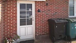 Una casa in mattoni con una porta bianca e un bidone della spazzatura.