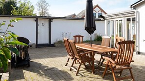 Eine Terrasse im Freien mit einem Holztisch, Stühlen, einem Grill und einem Sonnenschirm.