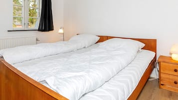 A double bed with a wooden frame, a bedside table with a lamp, and a window with curtains.