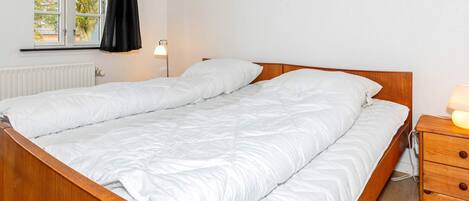 Un lit double avec un cadre en bois, une table de chevet avec une lampe et une fenêtre avec des rideaux.