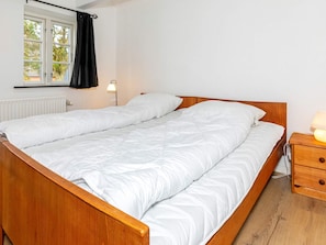 A double bed with a wooden frame, a bedside table with a lamp, and a window with curtains.