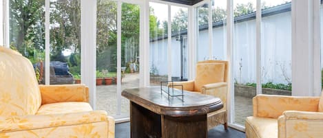 Un invernadero con techo de madera, ventanas grandes y mobiliario amarillo con estampado.