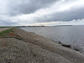 A gravel path beside a body of water with a cloudy sky.