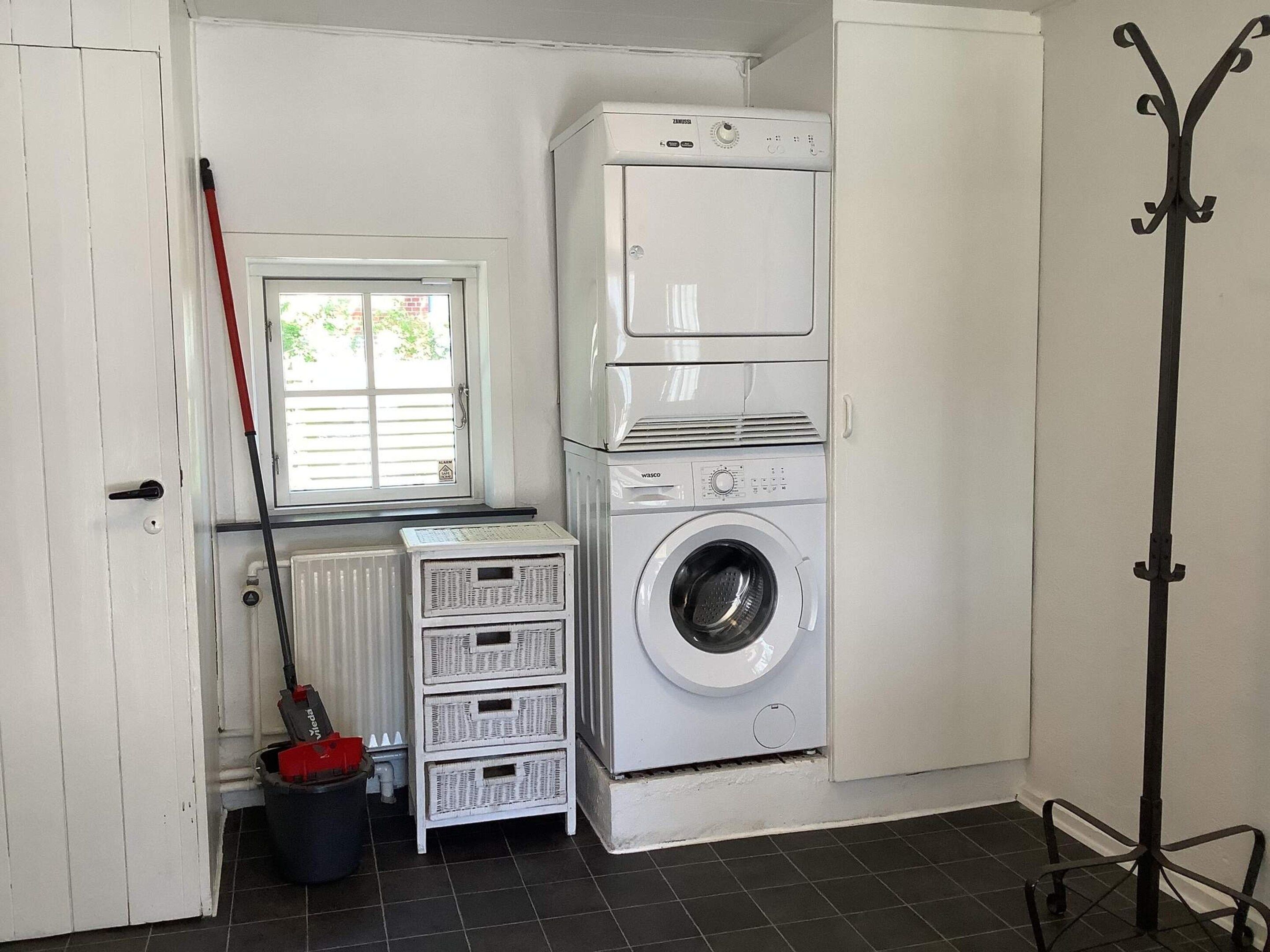 A laundry room with a front-loading washing machine, stacked drying machines, a mop, and a bucket.