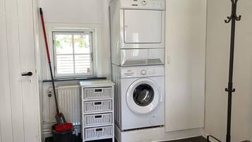 A laundry room with a front-loading washing machine, stacked drying machines, a mop, and a bucket.