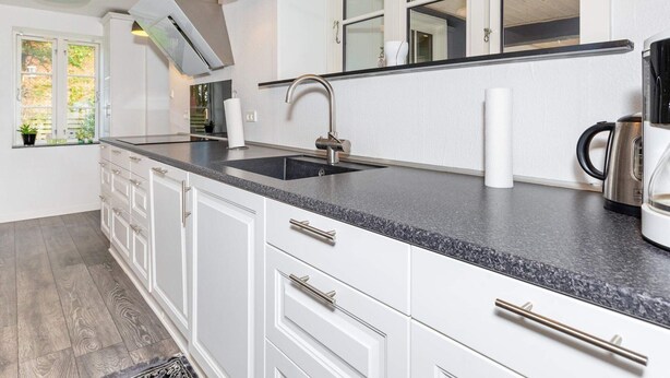 Una cocina moderna con armarios blancos, encimera de granito, pileta de acero inoxidable, lámparas colgantes y una cafetera.