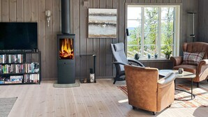 A cozy living room with a wood-burning stove, a bookshelf, a comfortable sofa, and a view of the outdoors through a large window. - 10 Person Holiday Home in Nesbyen-by Traum (Nes)