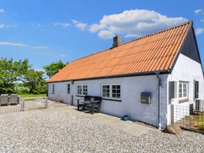 A single-story building with a sloped roof, a gravel driveway, and a fenced outdoor area.