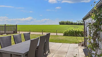 Een terras buiten met een tafel en stoelen, een uitzicht op een groen veld, en een hek.
