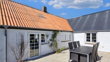 Een huis met een pannendak, een terras met een tafel en stoelen, en een witte buitenmuur.