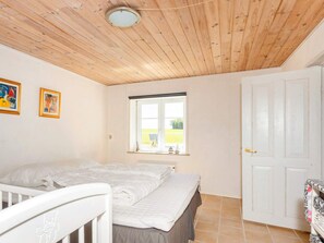 A room with a wooden ceiling, a bed with white bedding, a window with a view, and a white door. - 5 Person Holiday Home in Karby (Øster Assels)