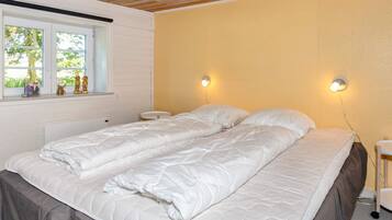 A double bed with a quilted mattress, a bedside table, a nightstand, and a window with a view of greenery.