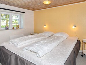 A double bed with a quilted mattress, a bedside table, a nightstand, and a window with a view of greenery.