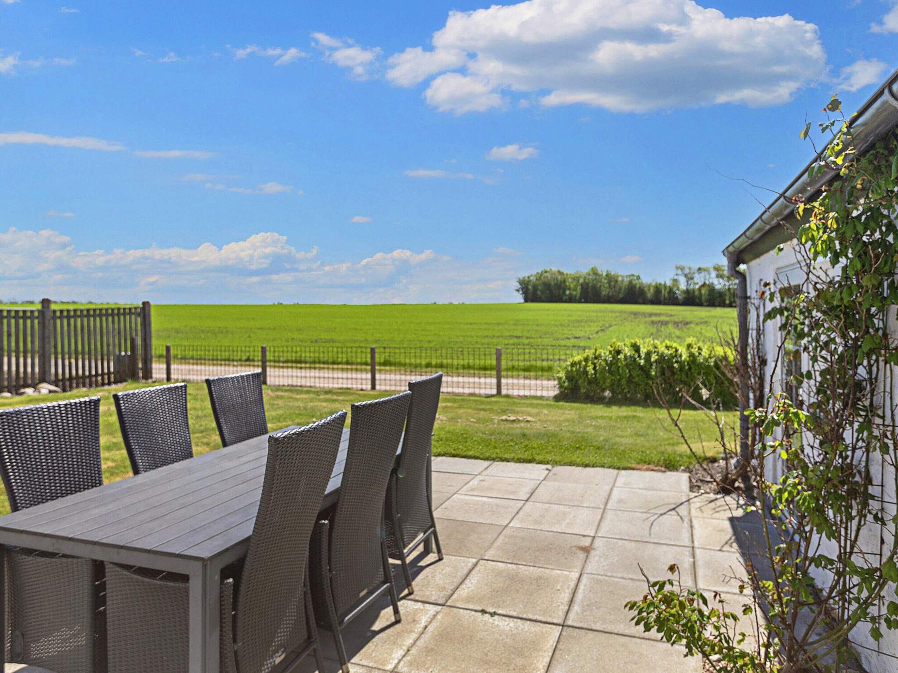 Een terras buiten met een tafel en stoelen, een hek en uitzicht op een groen veld.