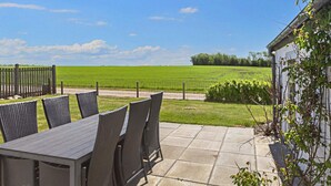 Un patio exterior con una mesa, sillas, una cerca y vistas a un campo verde.