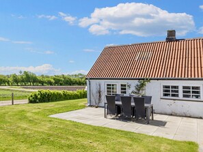 A house with a tiled roof, a patio with outdoor furniture, and a fenced yard.