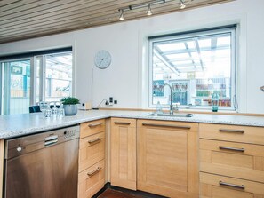A modern kitchen with wooden cabinets, a dishwasher, a sink, and a clock on the wall. - 12 Person Holiday Home in Thyboron (Thyborøn)