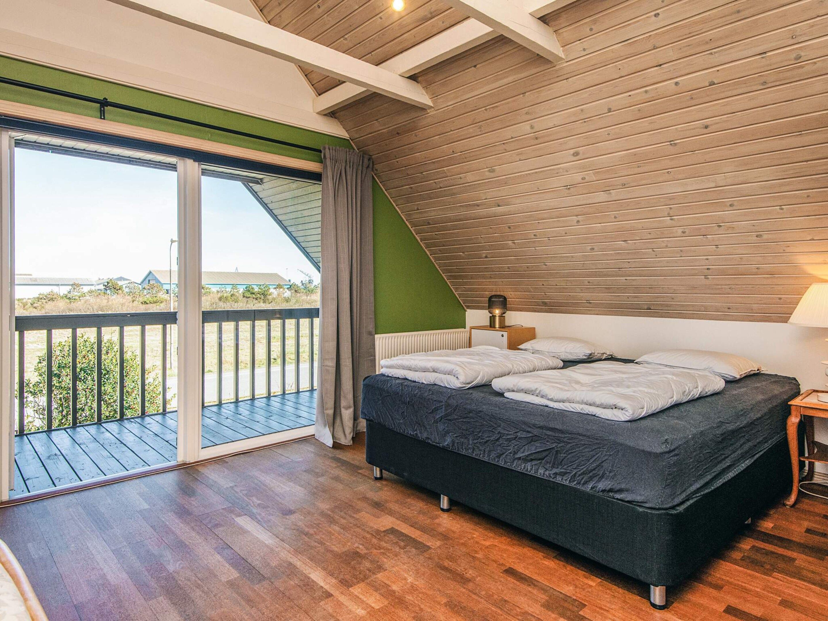 A bedroom with a large bed, a view through a sliding glass door to the outdoors, and a sloped ceiling.