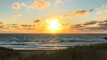 A sunset over the ocean with waves and grassy foreground.