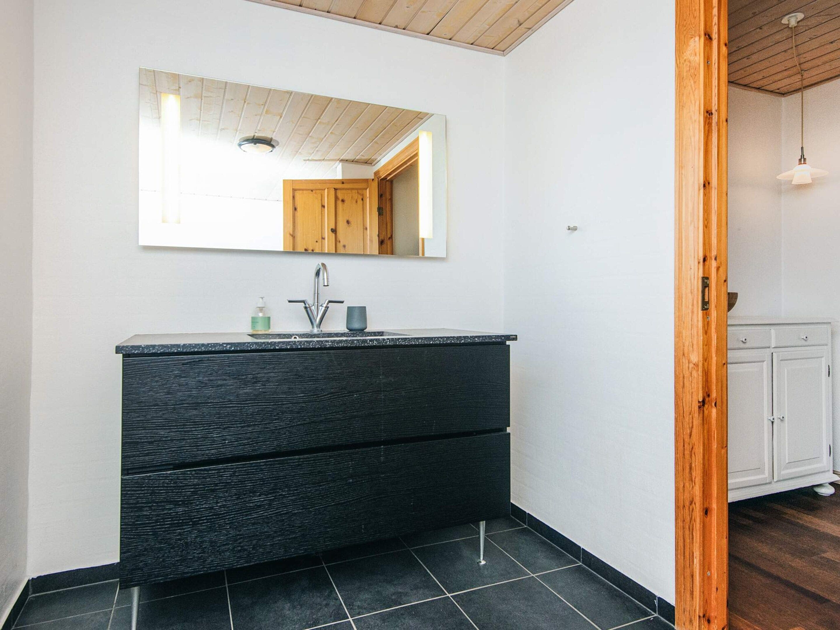 A bathroom with a black vanity, a mirror, and a wooden ceiling.
