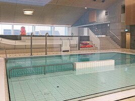 En indendørs swimmingpool med flisegulv, gelænder og trappe op til et saunaområde.
