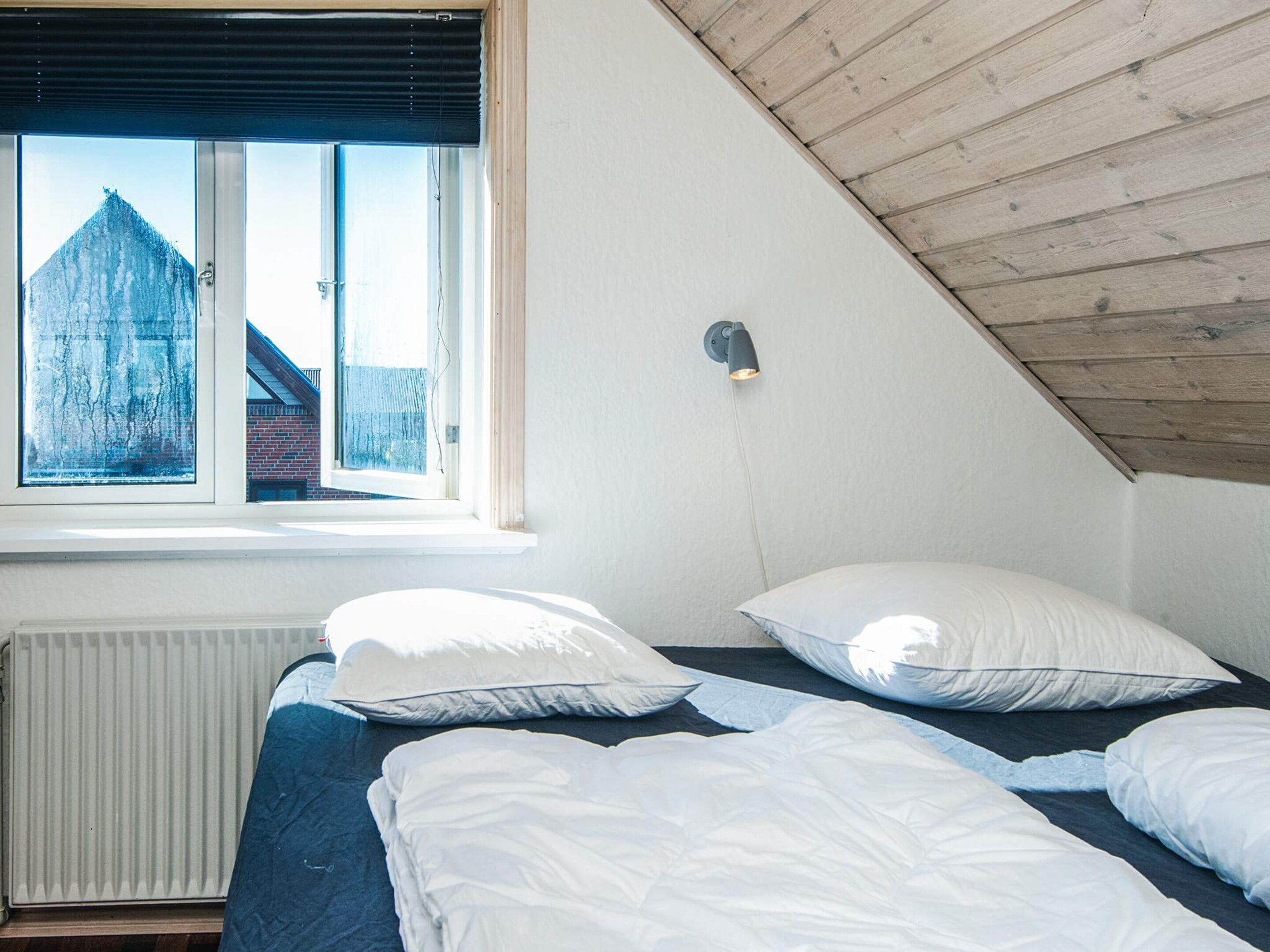 Una camera da letto con soffitto spiovente, una finestra vista edificio e un punto luce fissato al muro.