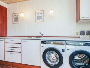 A modern kitchen with a built-in washer and dryer, wooden cabinets, and wall-mounted light fixtures. - 12 Person Holiday Home in Thyboron (Thyborøn)