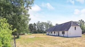 A white building with a sloped roof, surrounded by a grassy field and trees. - 6 Person Holiday Home in Laeso (Læsø)
