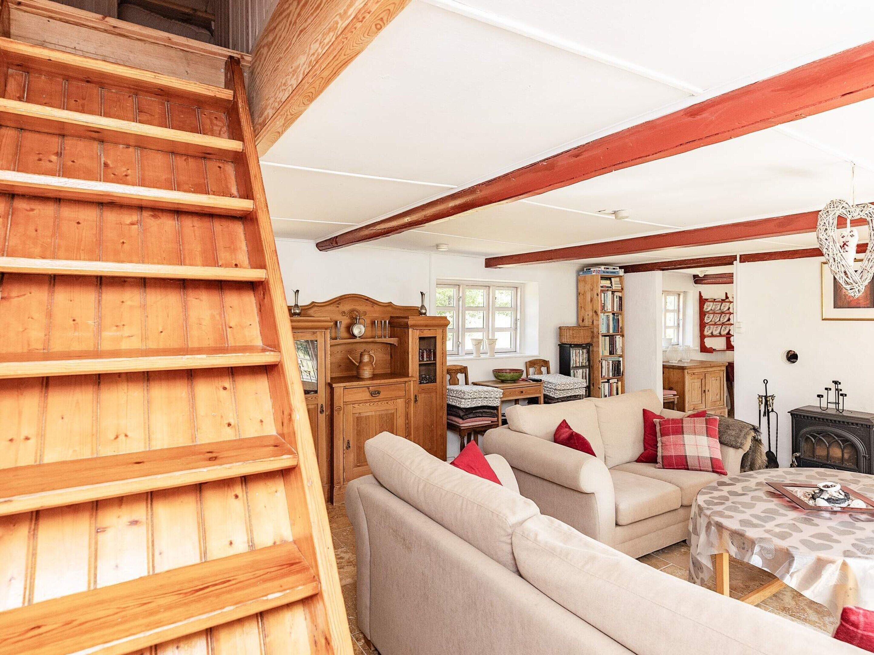 A cozy living room with a wooden staircase, a sofa set, a fireplace, and a bookshelf.