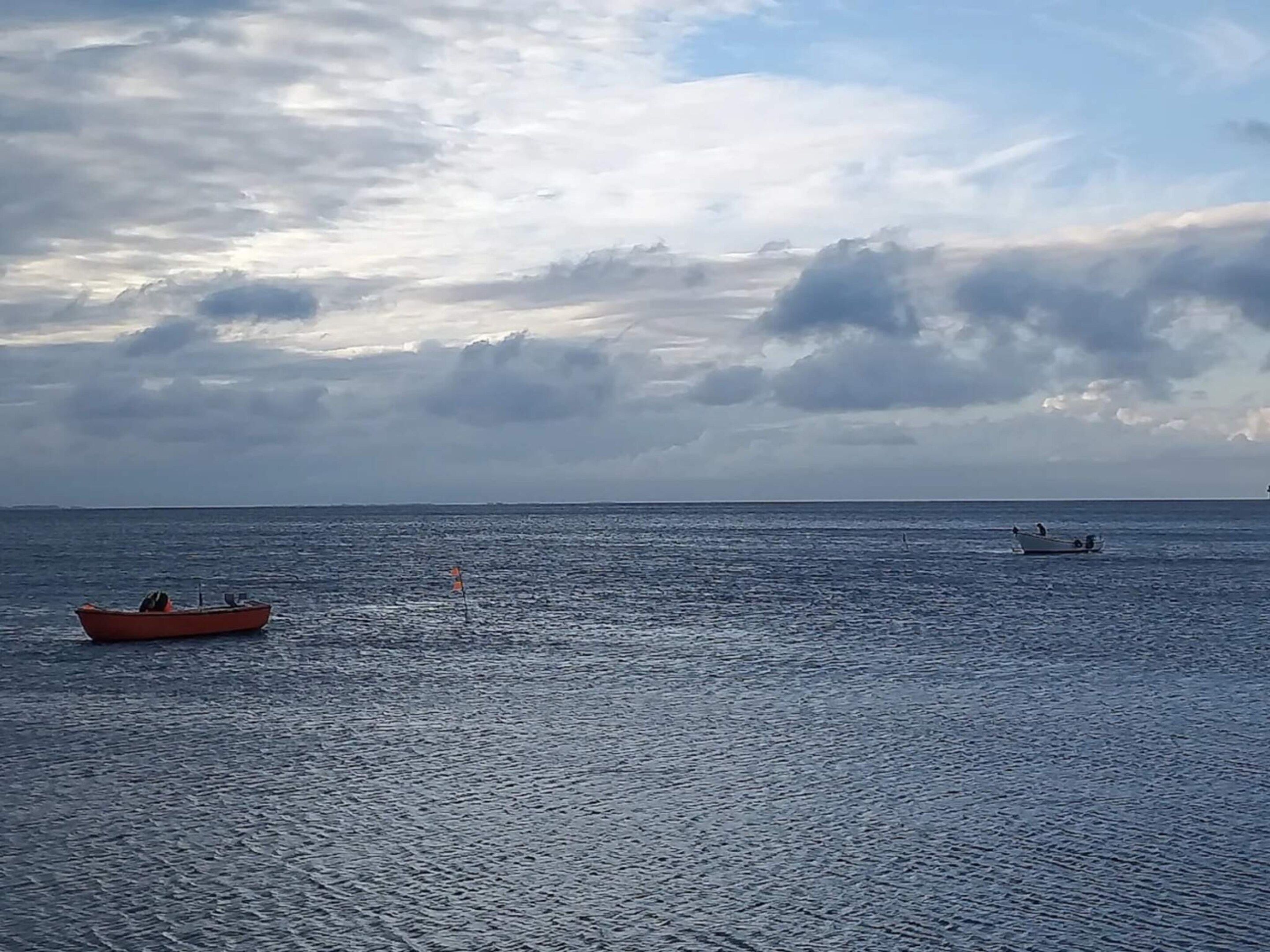 A calm sea with two boats, one orange and one white, under a cloudy sky.