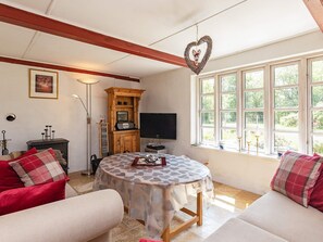 A cozy living room with a round table, red and beige sofas, a wooden cabinet, a television, and a window with a view of greenery. - 6 Person Holiday Home in Laeso (Læsø)