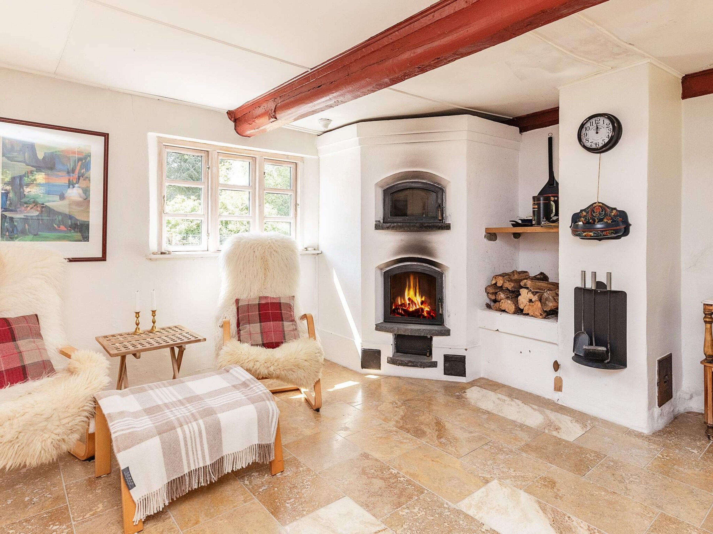 A cozy living room with a fireplace, a fur chair, a wooden table, and a painting on the wall.