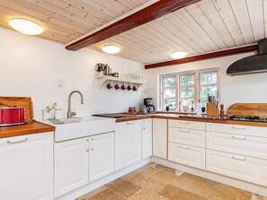 A kitchen with white cabinets, a red toaster, a sink, and a window with a view of trees. - 6 Person Holiday Home in Laeso (Læsø)