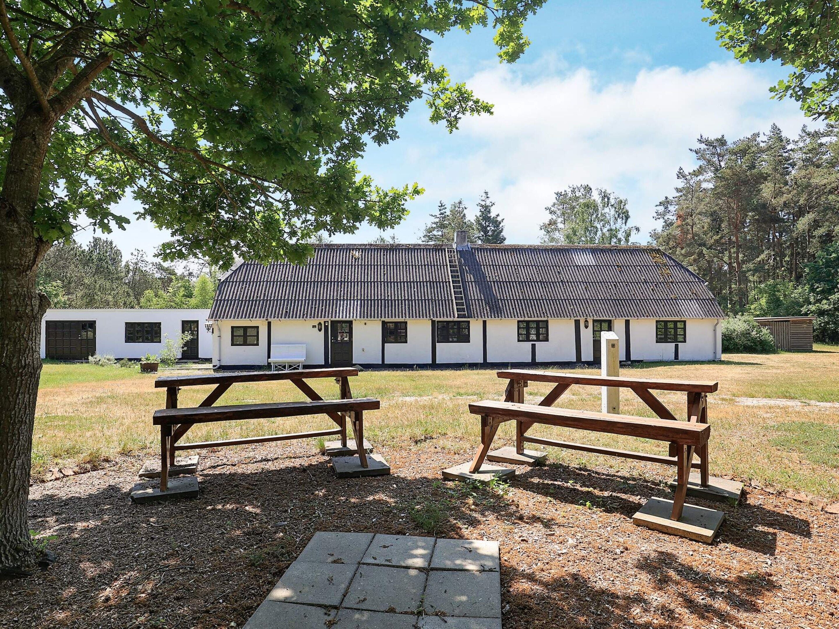 A rustic building with a tiled roof, surrounded by a grassy area with picnic tables.