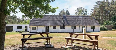 A rustic building with a tiled roof, surrounded by a grassy area with picnic tables.