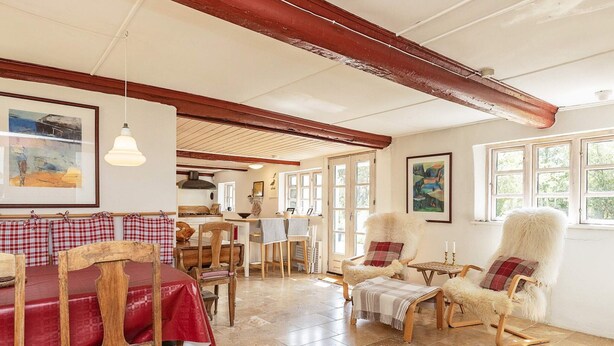 A cozy dining area with wooden furniture, a red tablecloth, and a view of the kitchen through large windows. - 6 Person Holiday Home in Laeso (Læsø)
