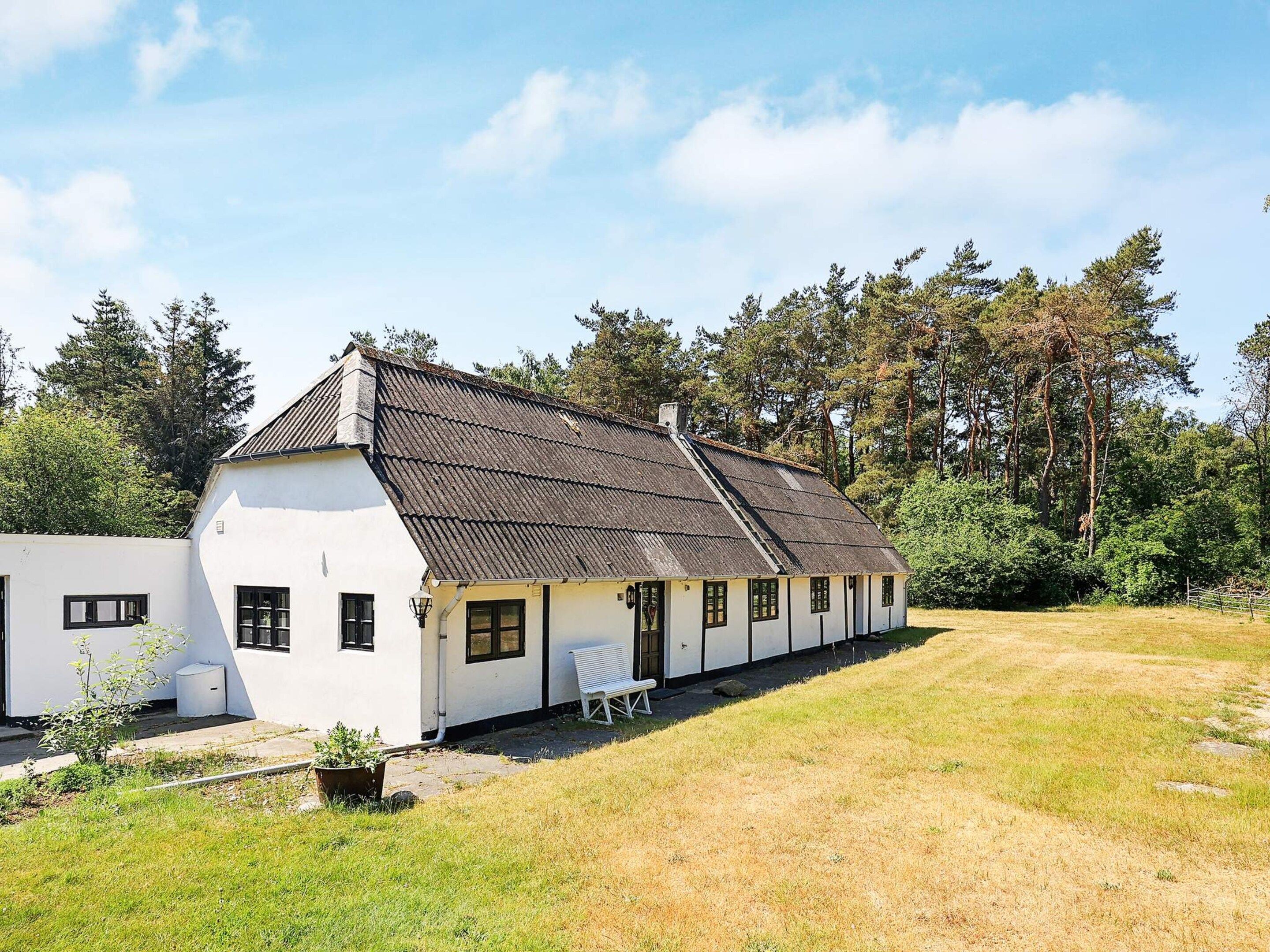 A white building with a sloped roof, a bench, and a grassy yard.