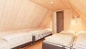 A cozy attic bedroom with wooden walls and sloped ceilings, featuring three beds and a small table. - 6 Person Holiday Home in Laeso (Læsø)