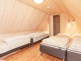 Un dormitorio abrigado en el ático con paredes de madera y techos inclinados, con tres camas y una mesita pequeña.