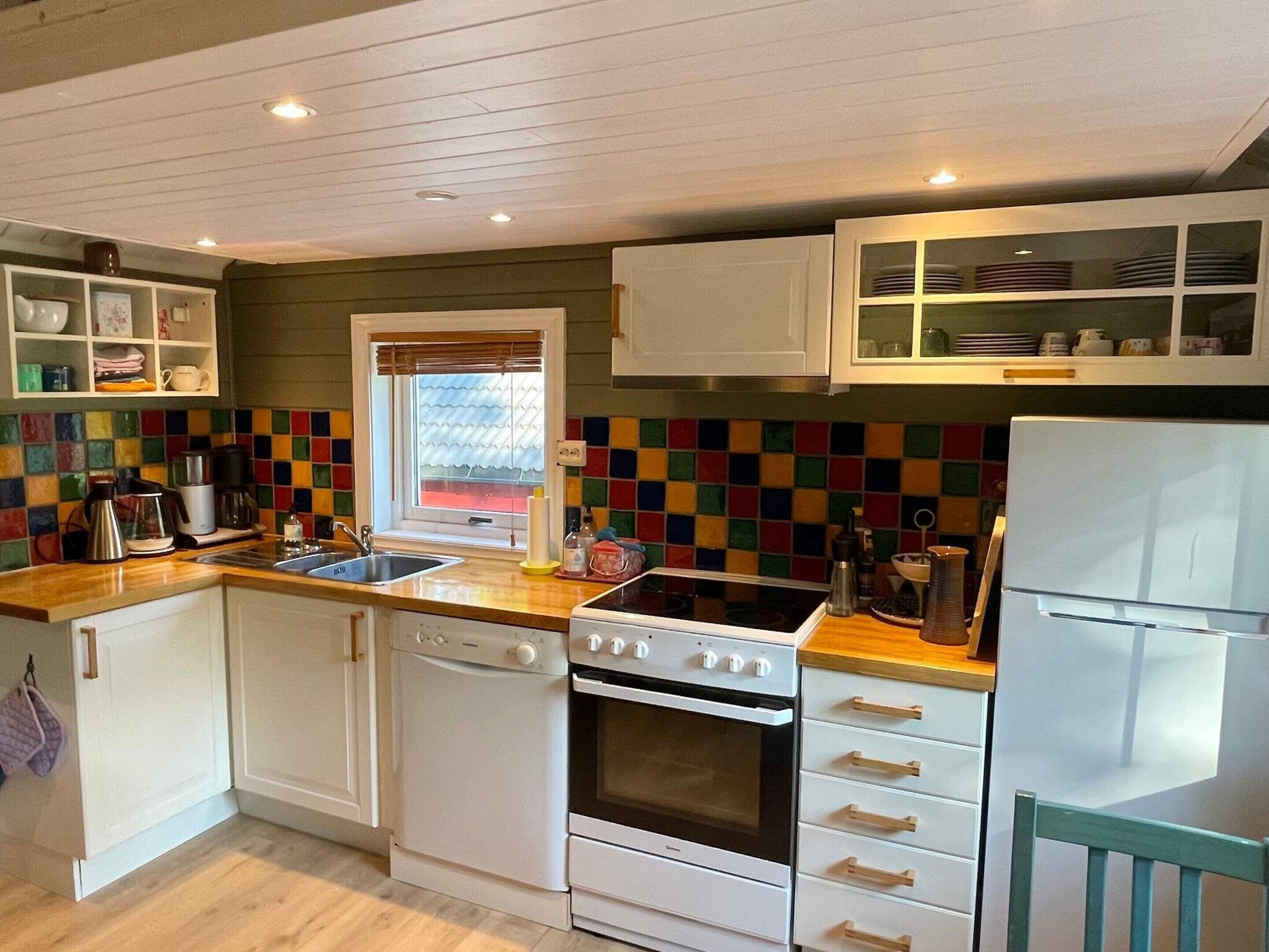A compact kitchen with white cabinetry, a colorful backsplash, a stove, and a refrigerator.